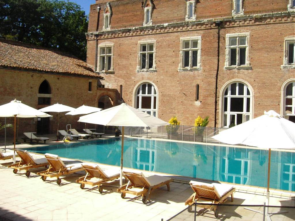 Piscine extérieure ensoleillée du Château de Terrides, entourée de chaises longues et d'espaces verts paisibles, offrant détente et bien-être au sein de ce somptueux hôtel historique et lieu de réception.
